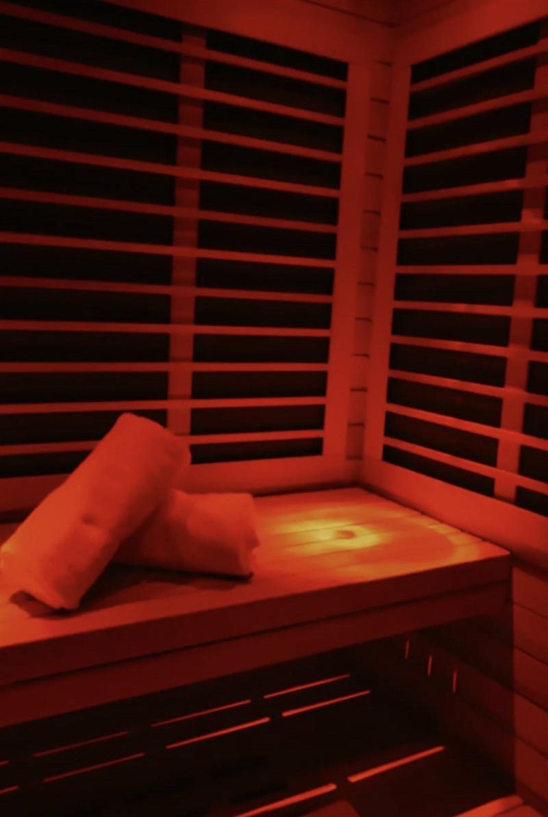 A private infrared sauna suite at Calor, glowing red, with rolled towels on the bench
